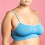 Big natural breasts in blue bra close-up on pink background, studio shot